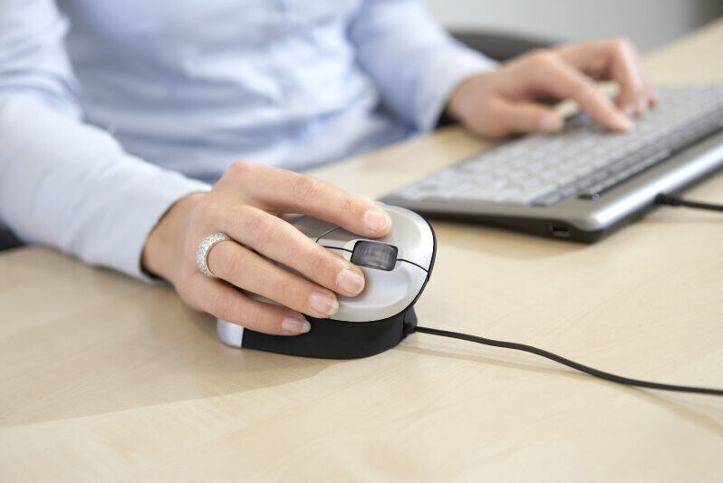 Een foto van een persoon die een ergonomische muis gebruikt, tijdens het werken.